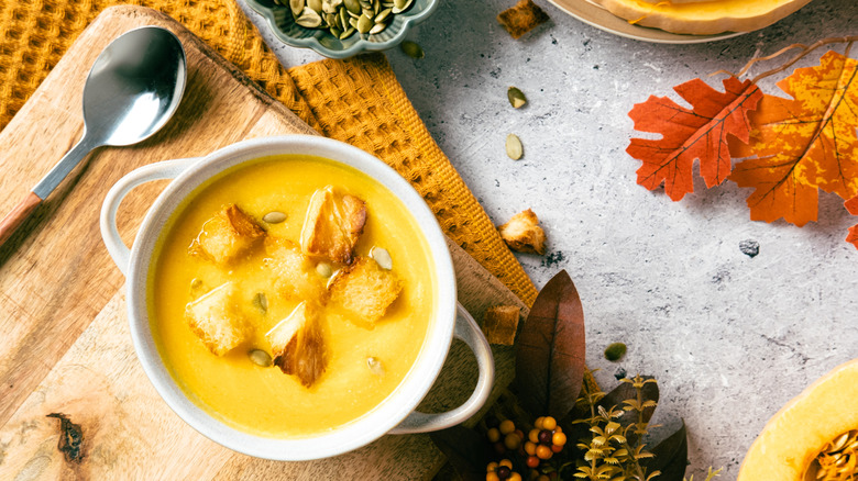 A white bowl of creamy pumpkin soup with croutons on top