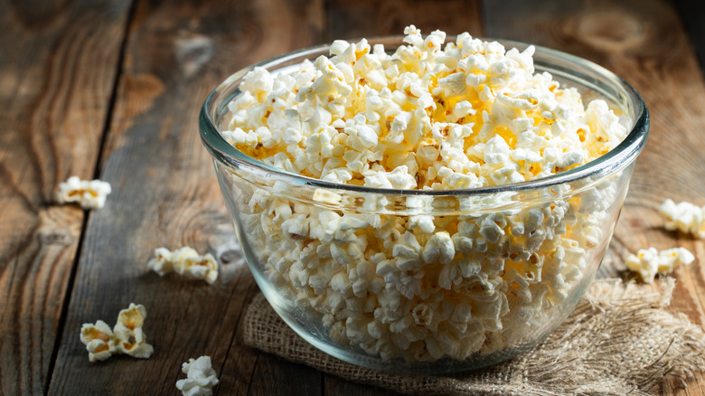 A clear glass bowl of popcorn on a wood table