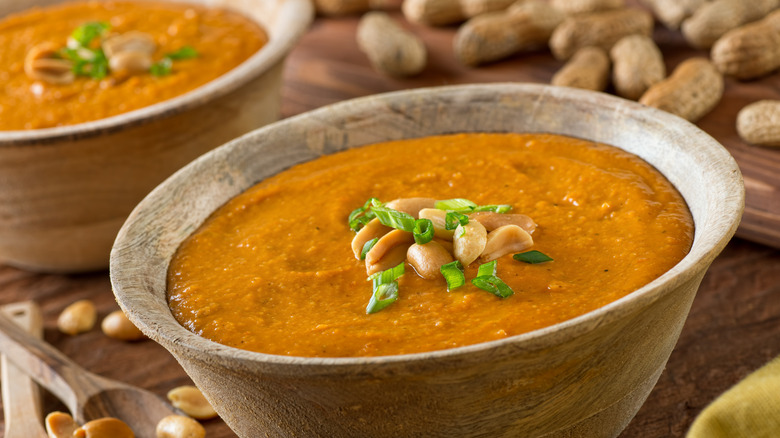 Peanuts on top of a creamy orange soup in a wooden bowl
