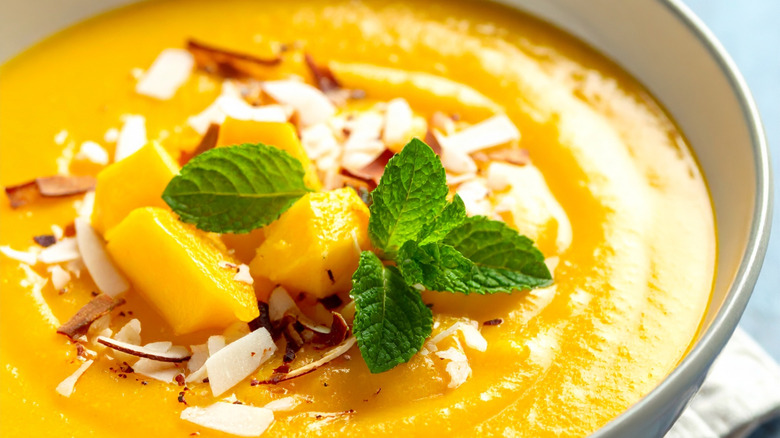 Close-up of a creamy yellow soup topped with mango and coconut