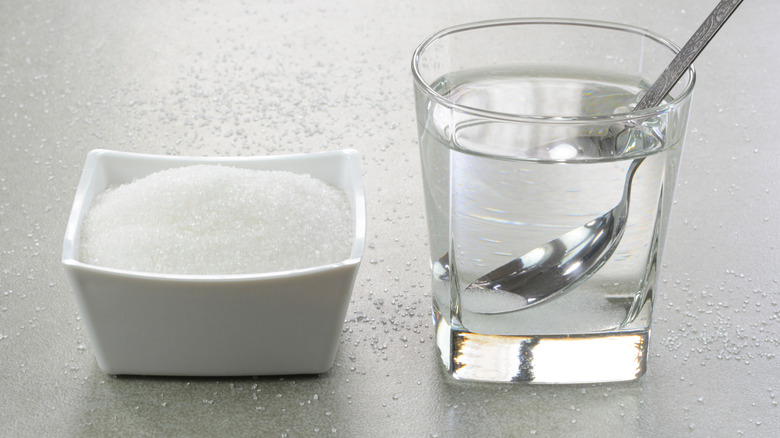 dish of sugar next to glass of water with spoon