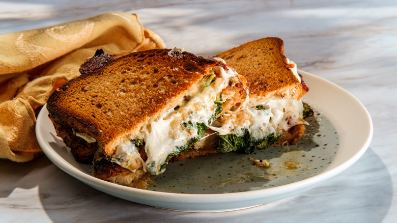 Two halves of a grilled cheese sandwich with kale on a white plate with a yellow cloth napkin