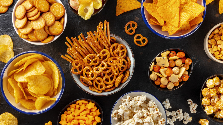 Pretzels, popcorn, and other snacks and crackers on a black background.