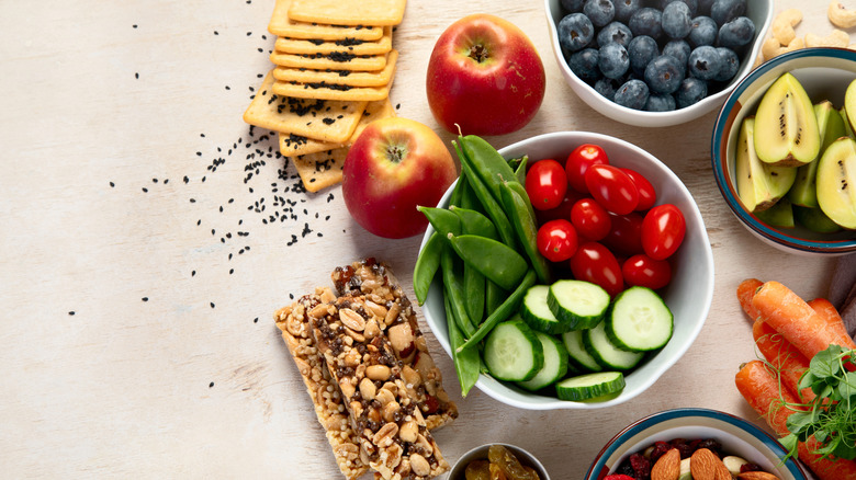 Apples, granola bars, and other healthy snacks spread out on a beige table.