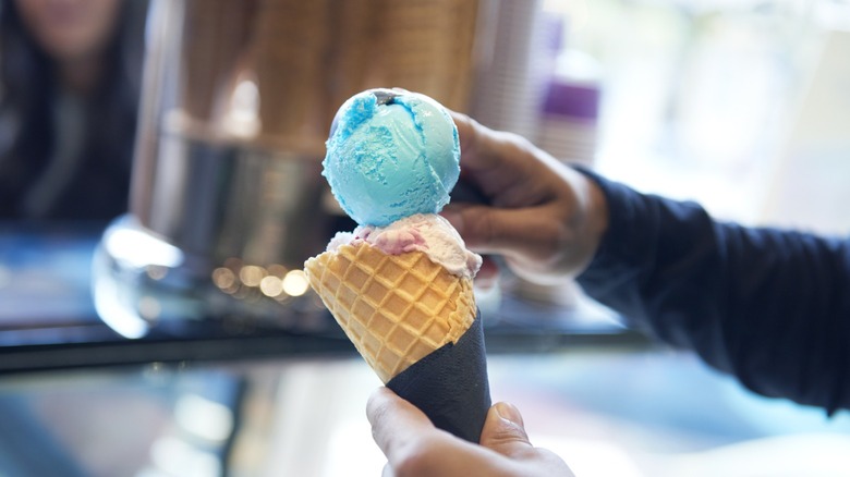 A person scooping blue ice cream into a cone.