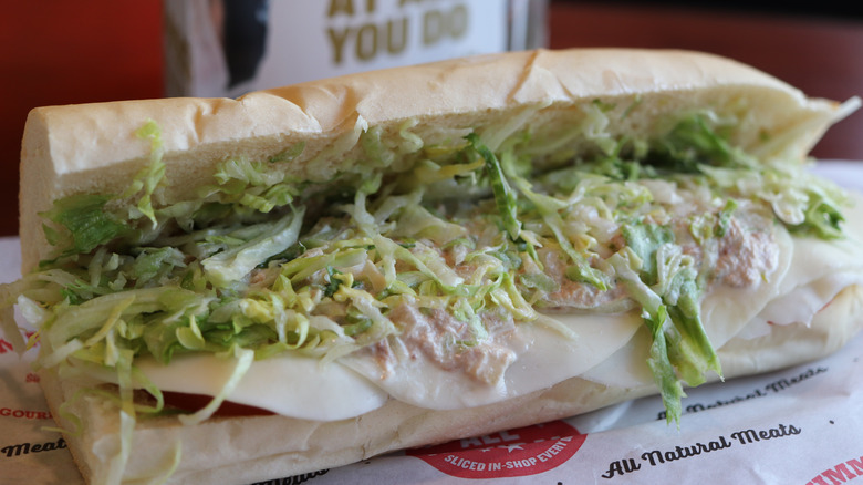 Close-up of a Jimmy John's sub sandwich filled with shredded lettuce, sliced cheese, and tuna salad on French bread.