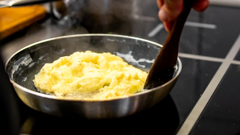 Person stirring scrambled eggs in pan over stove with wooden spatula