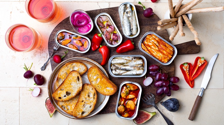 Tinned fish with bread and grapes on a board