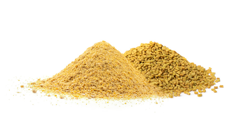 Two piles of ground and whole fenugreek seeds on a white surface.