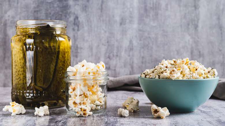 Popcorn in a bowl with dill and pickles displayed on a gray table.