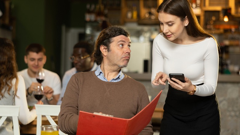 Customer holding restaurant menu with server pointing at it
