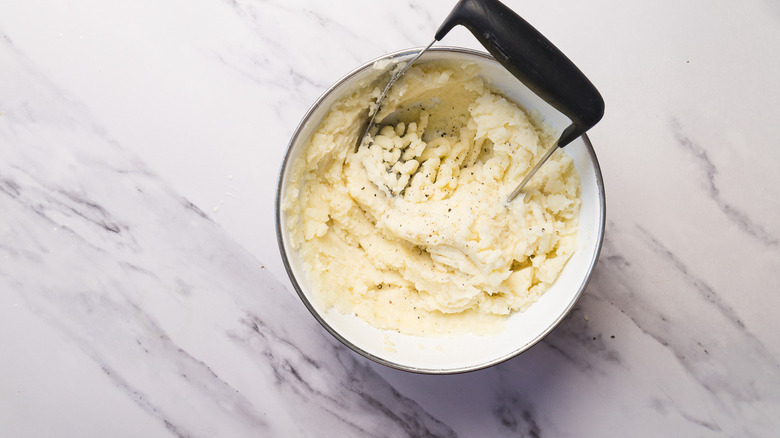 Mashed potatoes in bowl with masher