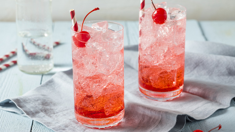 Two glasses of red tinted Shirley Temples sodas with straws and cherries