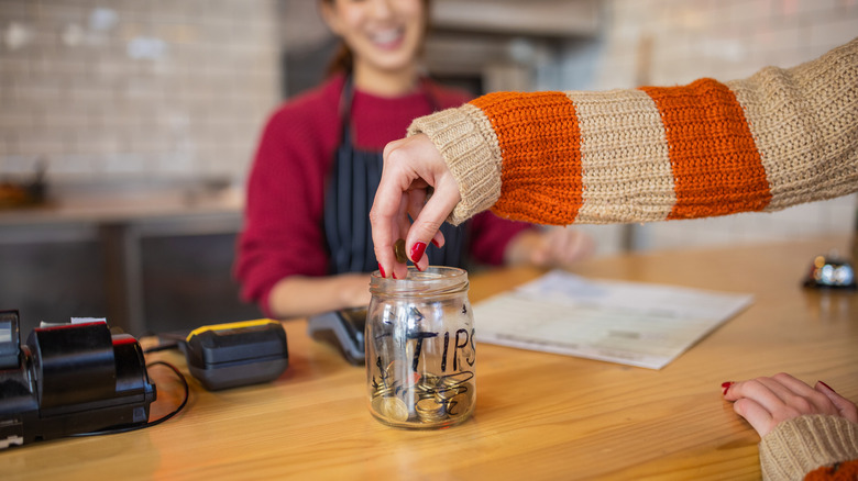 Hand dropping coins into a tip jar