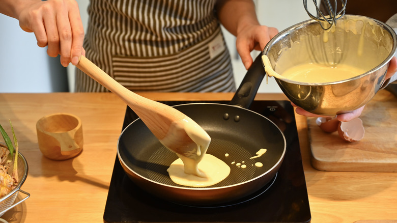 pouring pancake batter into pan with wooden spoon