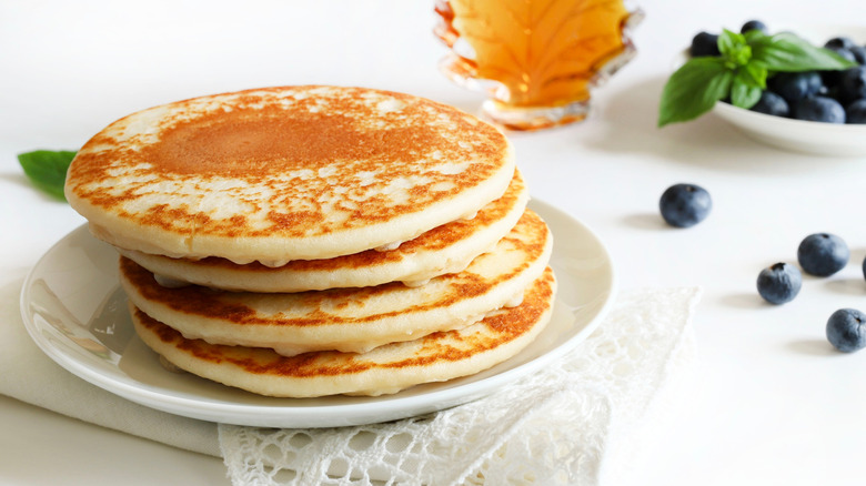 stack of pancakes on a white plate with blueberries and syrup nearby