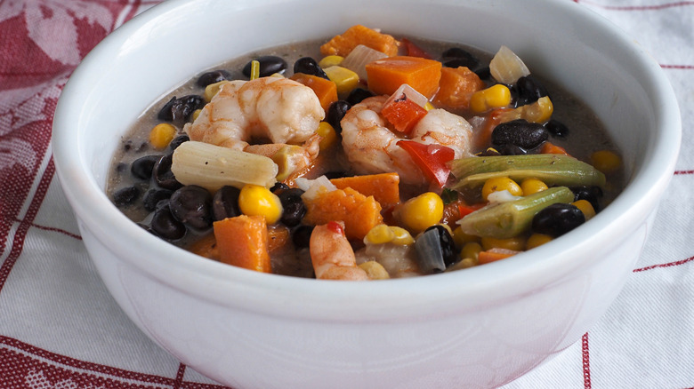 A black bean soup with shrimp served in a white bowl.