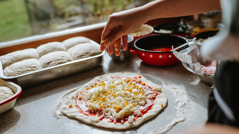 Person making a pizza with cheese and marinara sauce.