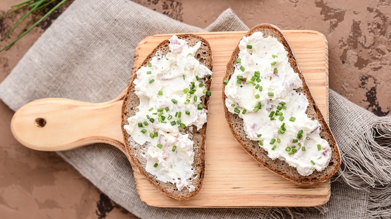 Wooden cutting board with two slices of bread topped with farmer cheese and chopped scallions
