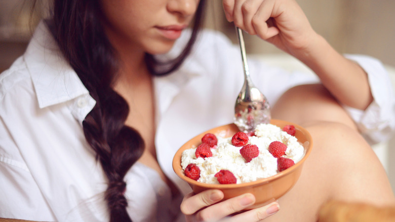 Woman sticking spoon into bowl of cottage cheese with raspberries on it