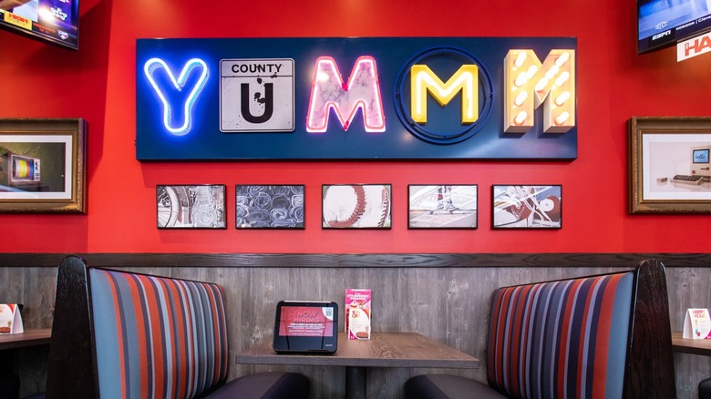 Empty booth in Red Robin restaurant underneath a neon sign reading yum