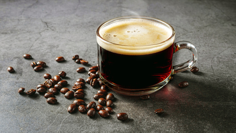 glass cup of espresso on a table next to coffee beans