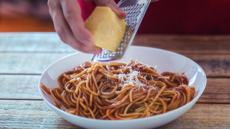 hands grating parmesan cheese over spaghetti