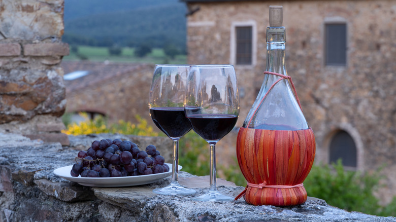 bottle and two glasses of chianti next to a plate of grapes