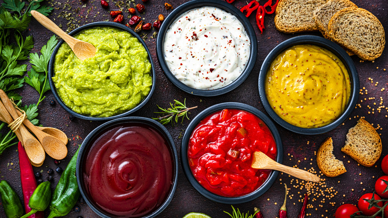 Assorted condiments in bowls on a table with bread and vegetables