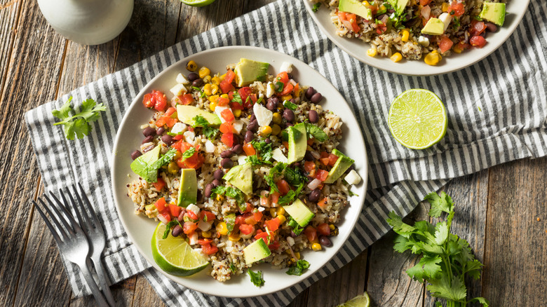 A quinoa burrito bowl topped with avocado, black beans, corn, and tomatoes