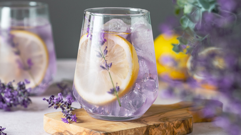 Glass of lavender lemonade garnished with a slice of lemon and a sprig of lavender sitting on a wooden board