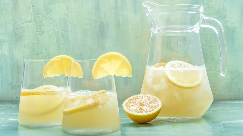 pitcher and glasses of lemonade with lemon slices and a half lemon