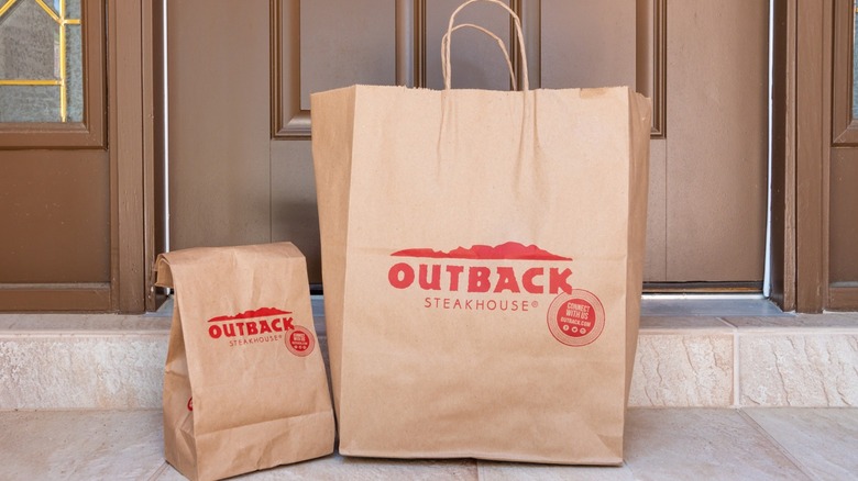 An Outback Steakhouse food delivery bag sitting in front of a house front entrance.