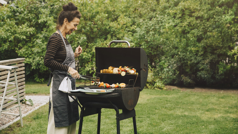woman grills chicken and vegetables outside
