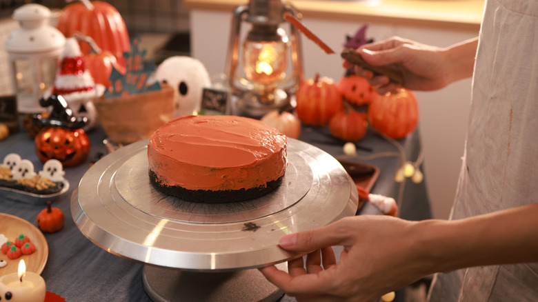 A person using a metal turntable to frost a Halloween-themed chocolate cake