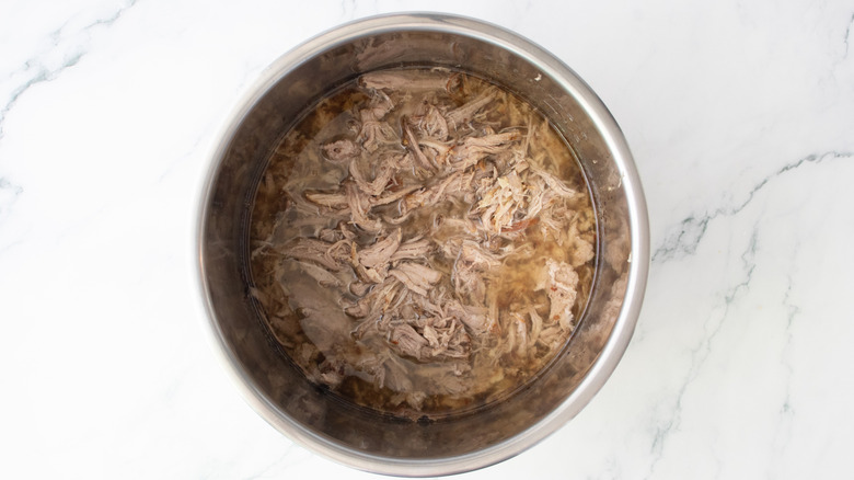 Pulled pork in a slow cooker pot with pan drippings