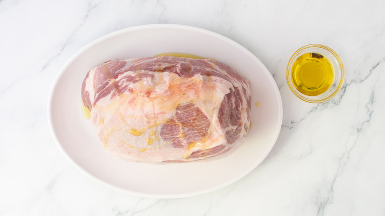 Raw pork butt drizzled with olive oil on a white platter