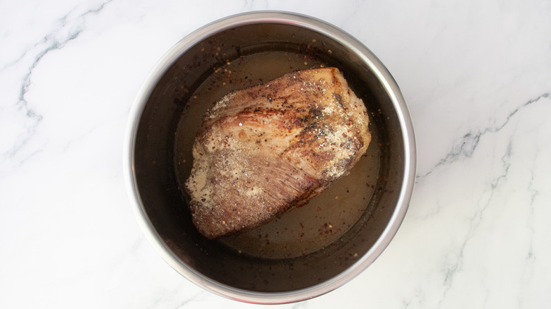 Seared pork butt, vinegar, and seasoning in a slow cooker pot