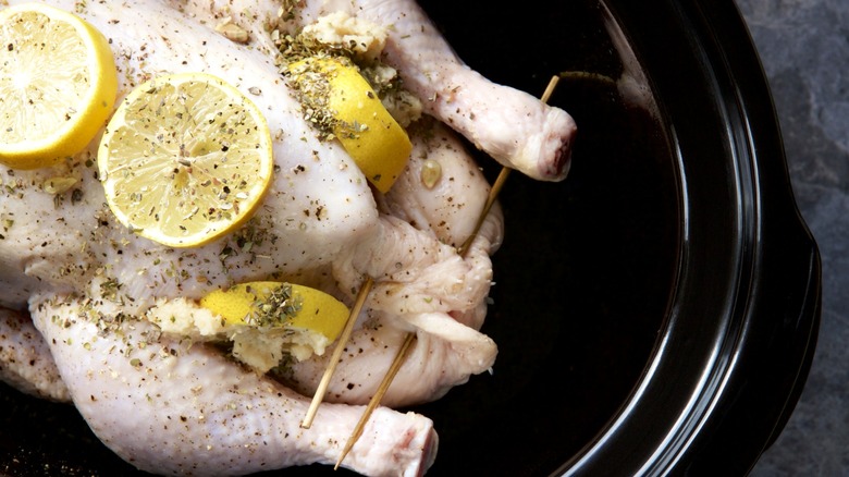 Whole raw chicken in slow cooker with lemon slices and seasoning