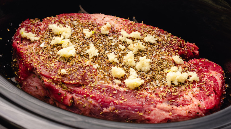 A cut of steak with seasonings sitting in a slow cooker