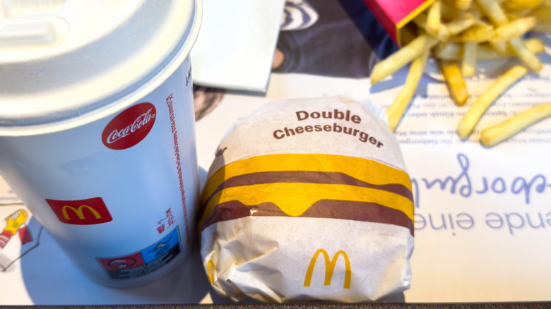 A double cheeseburger at McDonald's in paper wrapper next to takeout coffee and side of fries on tray