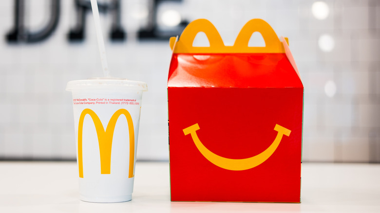 A red happy meal box sits on a white table, a white McDonald's takeout cup to the left.