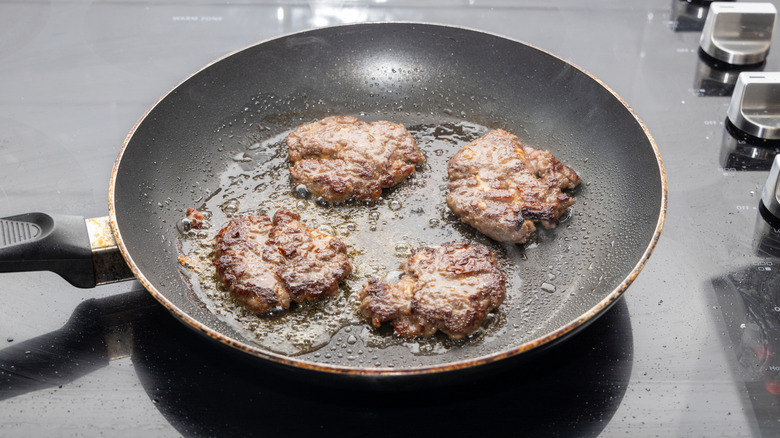 Burgers cooking in a nonstick pan.