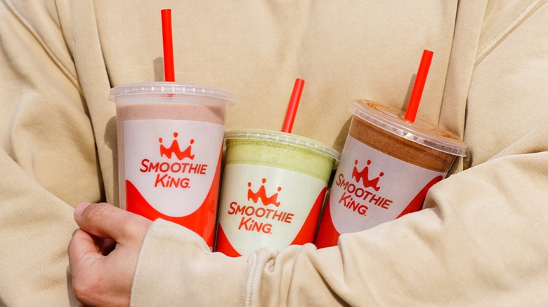 Person wearing sweatshirt holding three Smoothie King smoothies