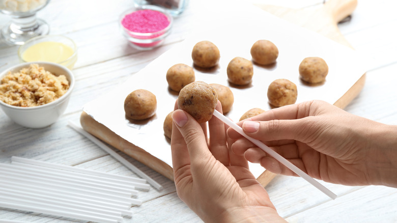 Hands inserting stick into cake pop ball