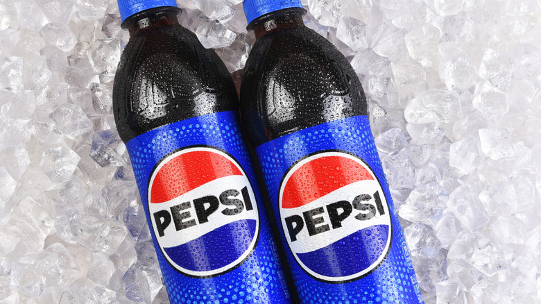 Two Pepsi bottles laying on ice cubes