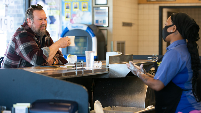 A man sitting alone at the front counter of Waffle House speaking to a cook and drinking coffee
