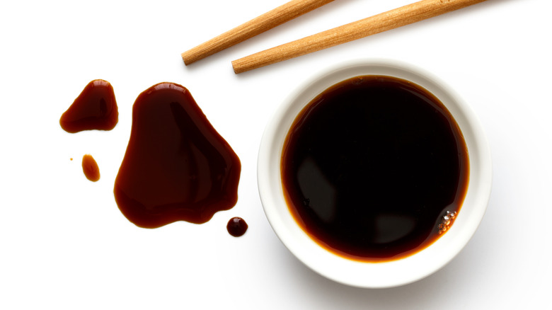 A bowl of soy sauce with chopsticks on a white background.