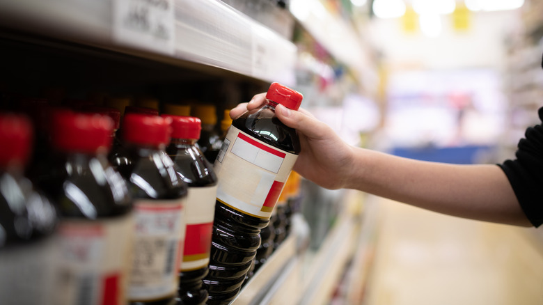 A shopper taking a bottle of soy sauce from a shelf