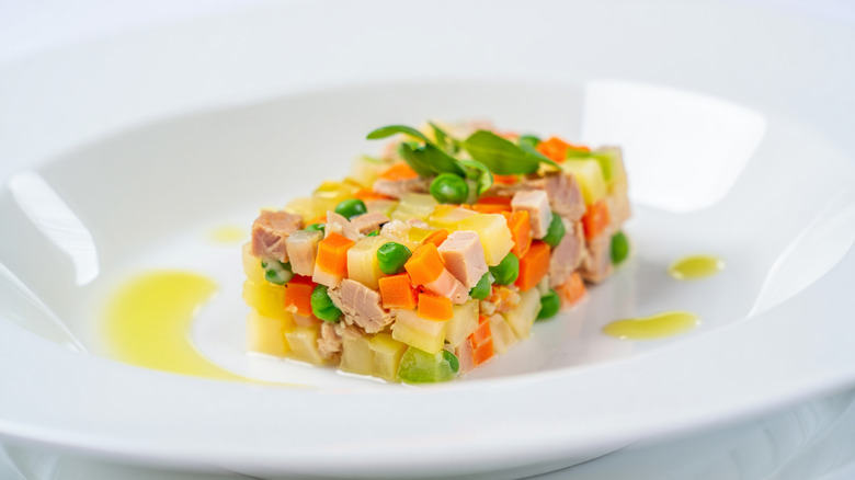 A classic ensaladilla rusa or Spanish potato salad plated in a white bowl as a rectangle with drizzles of oil around it.